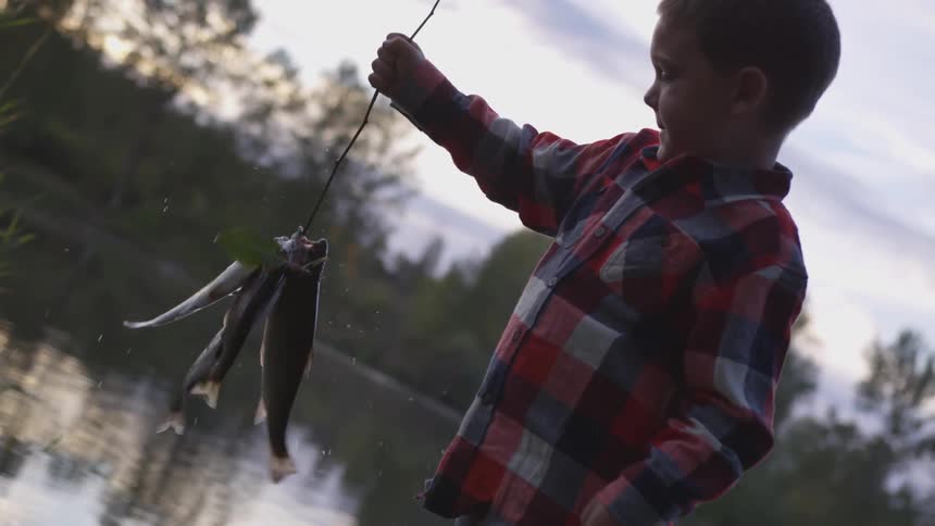 A boy holding fishes on a stick at sunset next to a river
