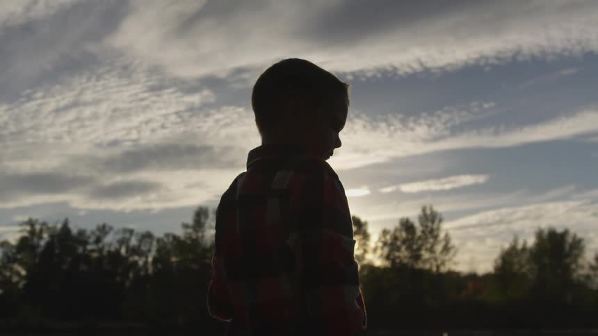 A young boy is seen standing in a forested area while holding a fishing rod