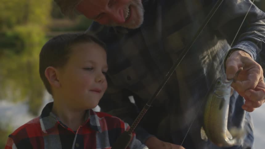 A dad smiles as he holds the wiggling fish his young son caught