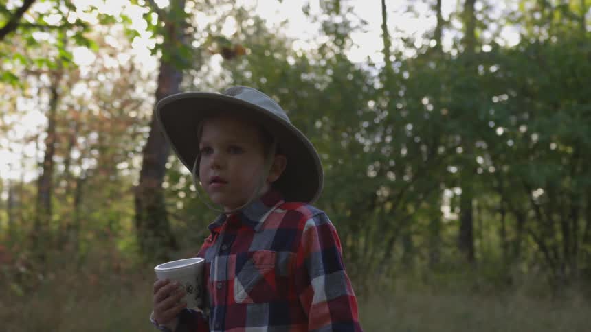 A boy walks past trees while carrying a container on a sunny day