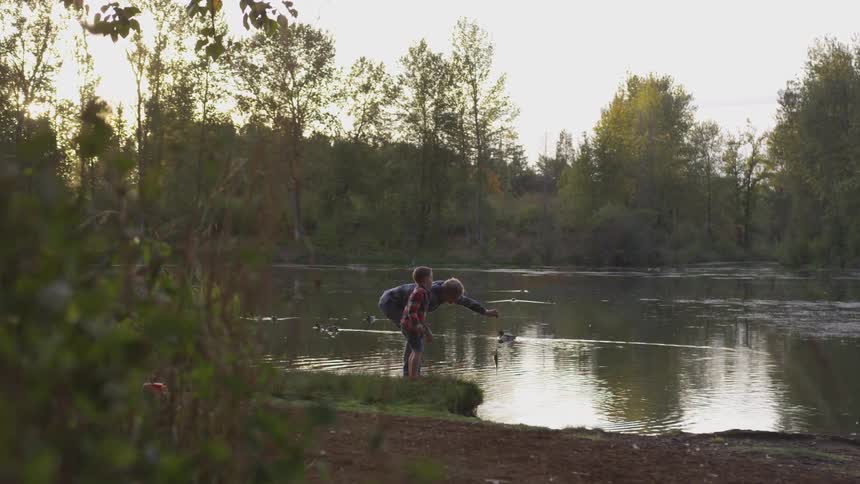 A man and his son standing at the edge of a river fishing