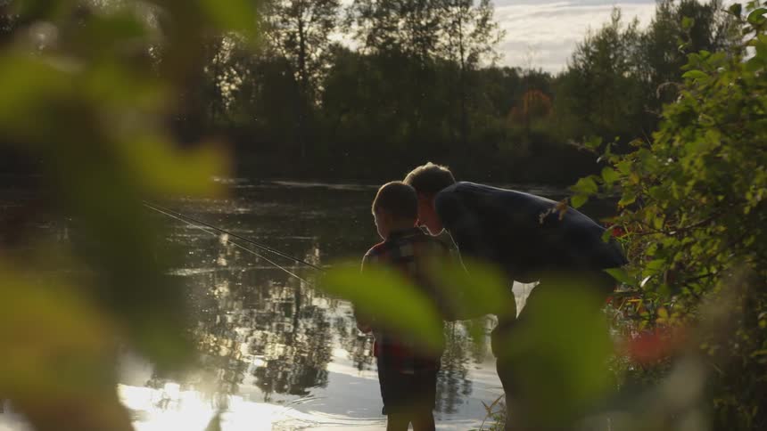 Father instructs son how to fish by a lake