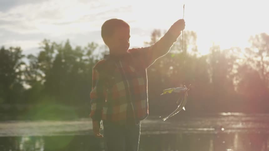 A boy holds up a fishing line with a caught fish by the river