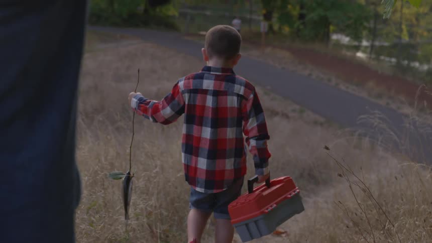 Father and son walk with fishing poles through grass