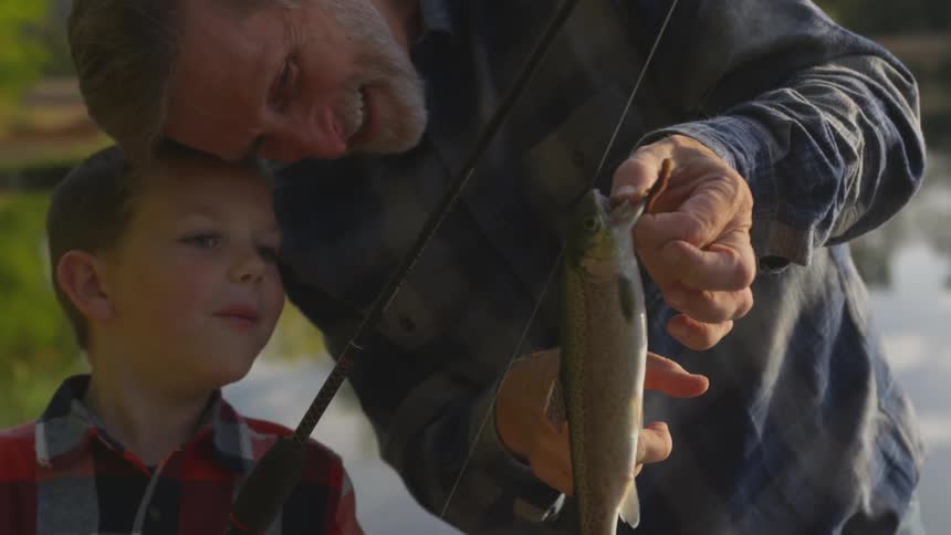 Father and son contemplating a recently caught fish at a river bank