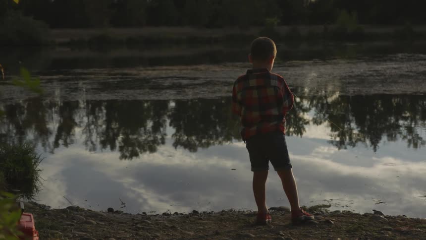 Boy stands near river fishing