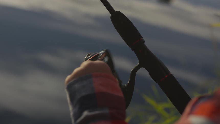 Person in flannel jacket winds fishing rod
