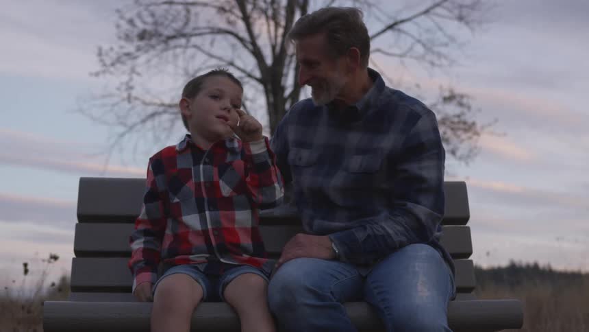 Father and son are sitting on a bench outside