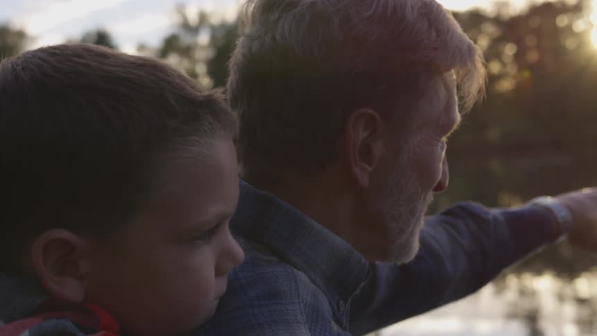 Father points out something across lake to son at sunset