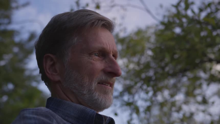 Man wearing striped blue shirt has a distant look in his eye in woods