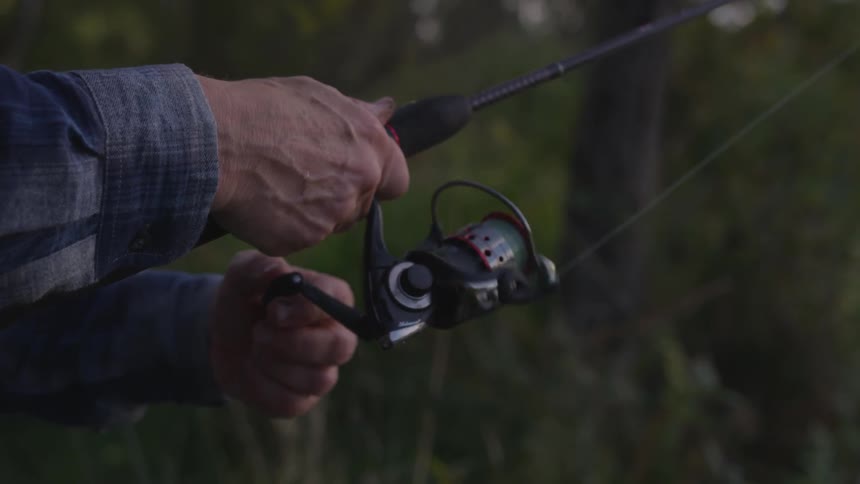 Man spools a spinning reel in forest at dusk