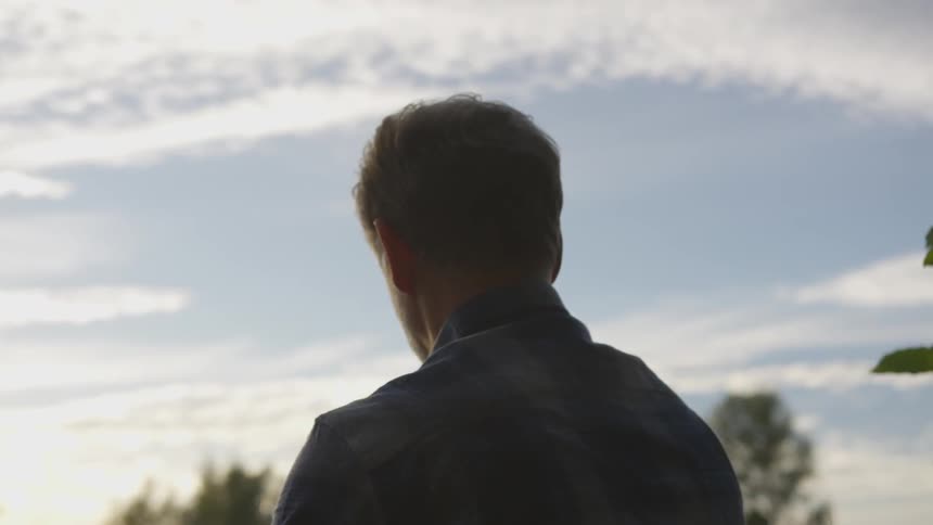 A gray haired man standing near trees looks out at the sky