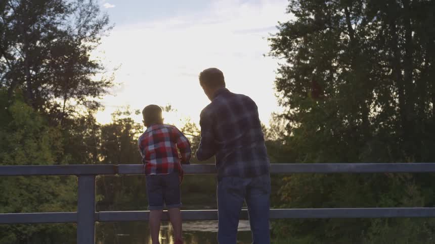 Father and son fishing on a river from a bridge in the morning