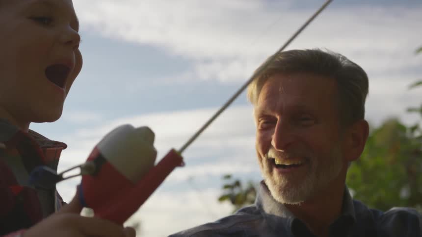 A young boy holding a fishing rod is learning how to fish from an older man with gray hair
