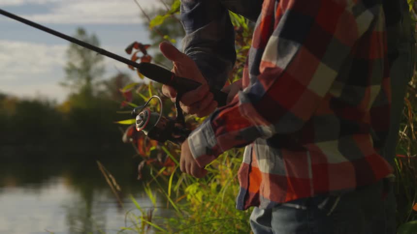A man reeling in a fishing reel on the edge of a river