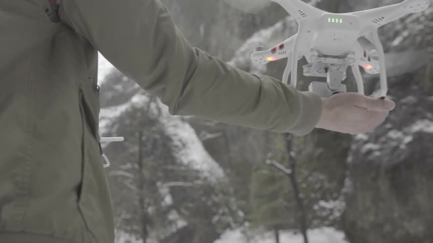 Man holds drone in one hand and controller in the other at base of snow covered mountain