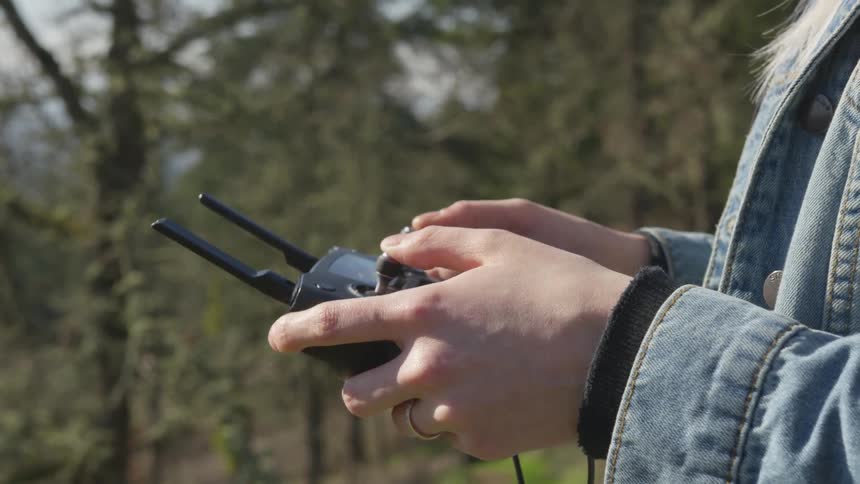 Blonde woman wearing denim jacket controls drone in forest on a sunny day