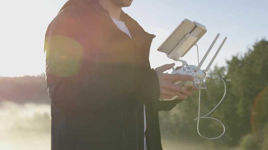 A man holds the controller to a drone while standing on a high point of a mountain or hill