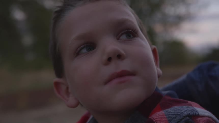 A young blue eyed boy looks up and then to the right at sunset