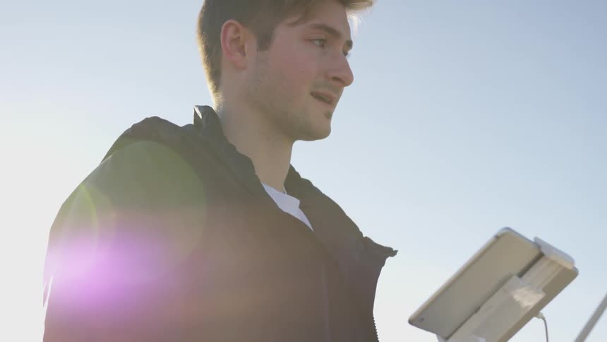A man in a dark jacket looks down at a tablet computer device and then slowly casts his gaze upwards