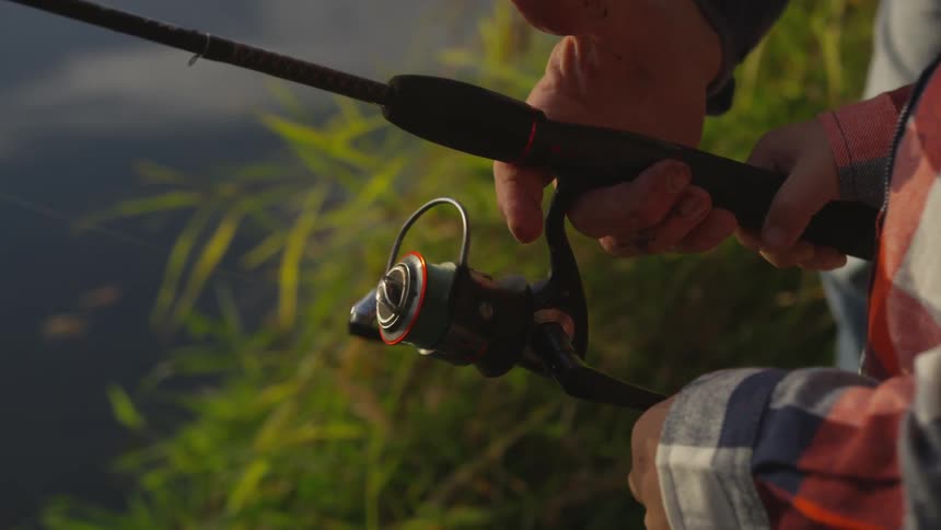 Man helps boy having colorful shirt on spool a spinning reel by the lake