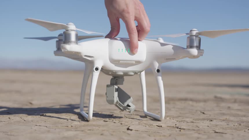 The hand of a person reaches down to press the power button on a small white drone with four propellers