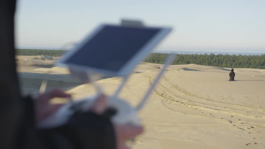 Person uses a screen mounted remote controller while standing in a desert on a sunny day