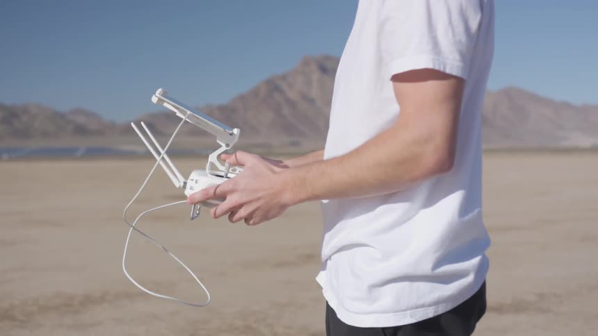 Man wearing white t shirt holds the remote controller in desert on a sunny day