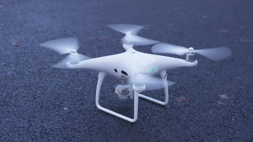 The four propellers of a white drone spin while it stays planted on the asphalt