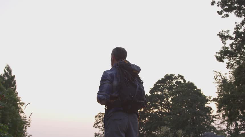 Man with backpack on stands looking out at the land below