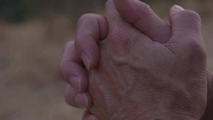 White hands are clasped together with fingers intertwined