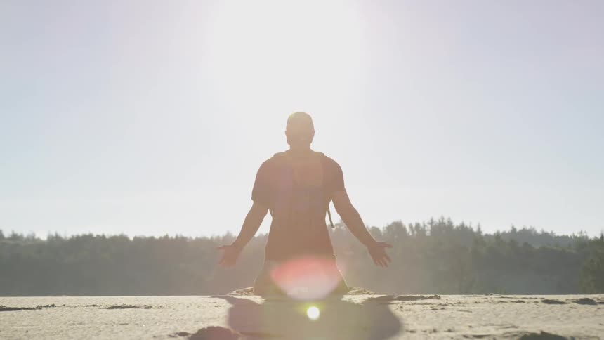 Man kneels in desert while the sun goes down