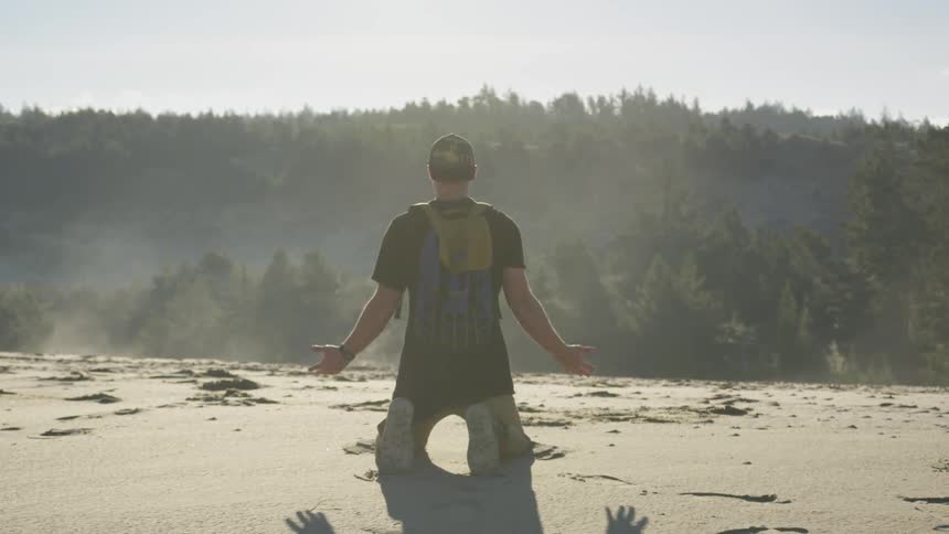 Man falls to knees on sand facing trees and sky