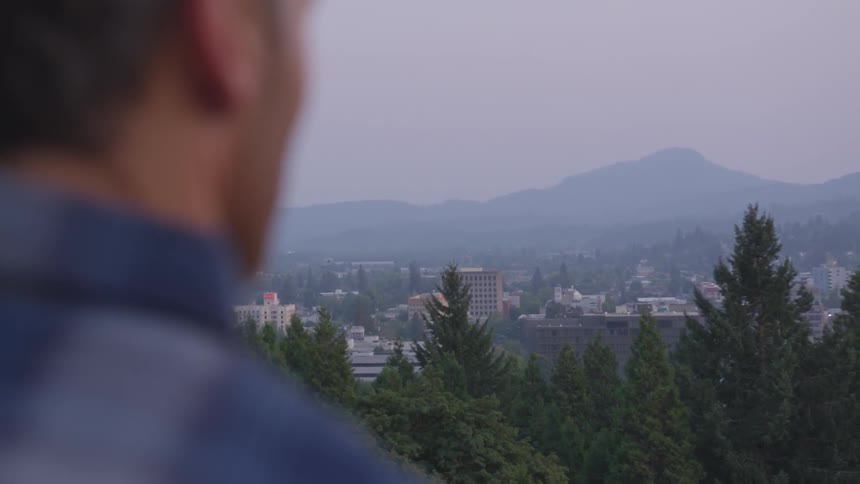 Man wearing striped shirt looks at the city and distant mountains at dusk