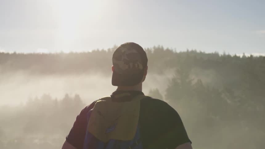 A man standing at the edge of a river at the base of a mountain in the forest