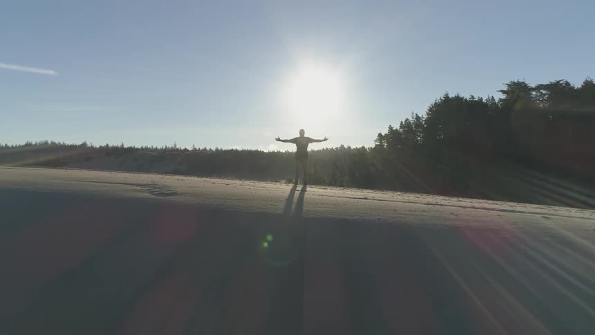 Man spreads arms under bright sun on sandy hill near trees