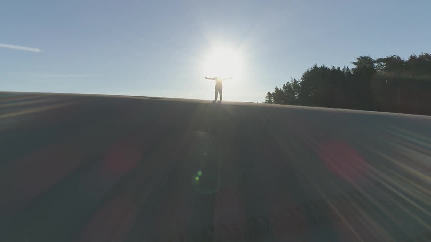 A man stands with his arms outstretched on the ridge of a sand dune as the sun shines around him