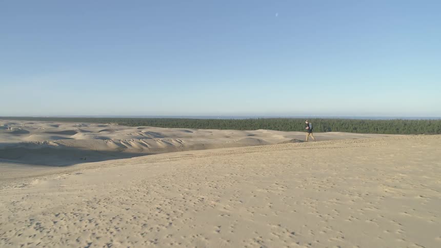 Man wearing backpack walks in the desert while the sun goes down