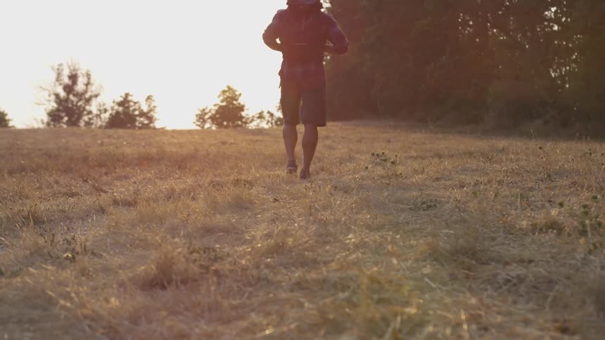 A man carrying a backpack hikes through a field towards a forest