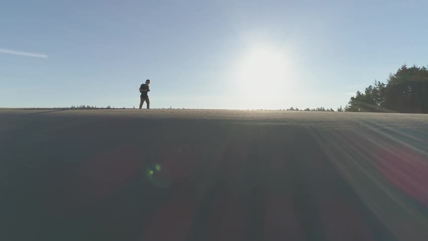 Man walks across sand dunes on a sunny day towards the trees