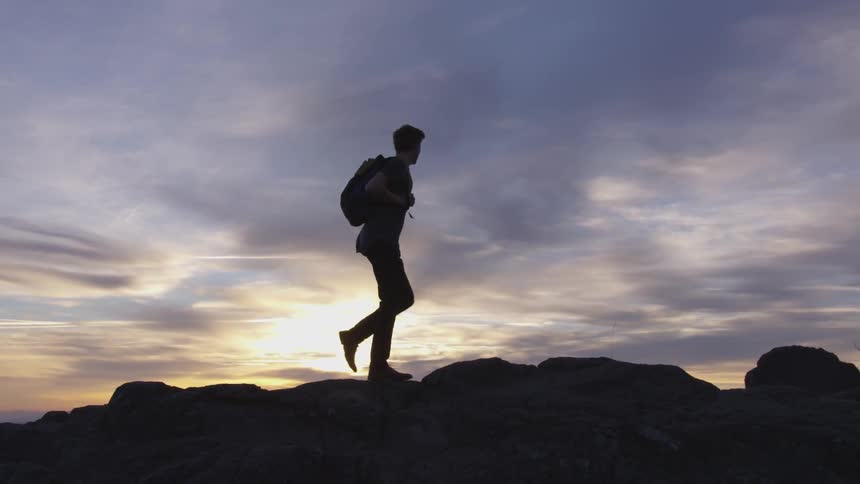 Man backlit by sunrise walks across rocks