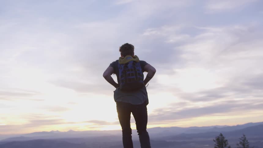 Person with backpack on is standing on top of a hill looking out into the horizon