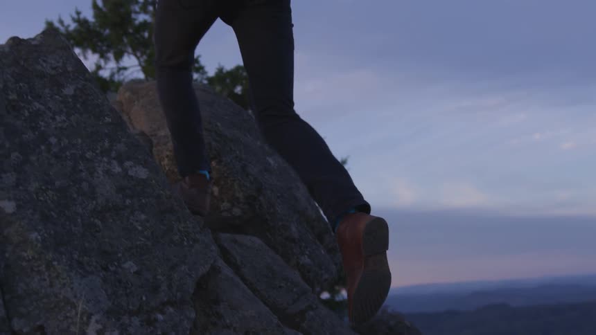 A man walks up rocks on the side of a mountain