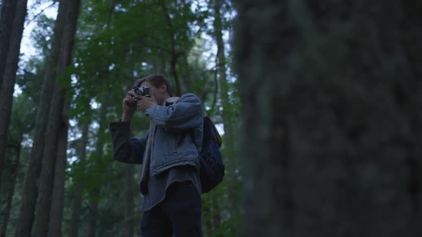 Man with a camera to his eye standing in a forest
