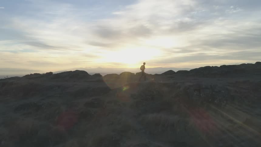 A man walking through a grassland at the top of a mountain