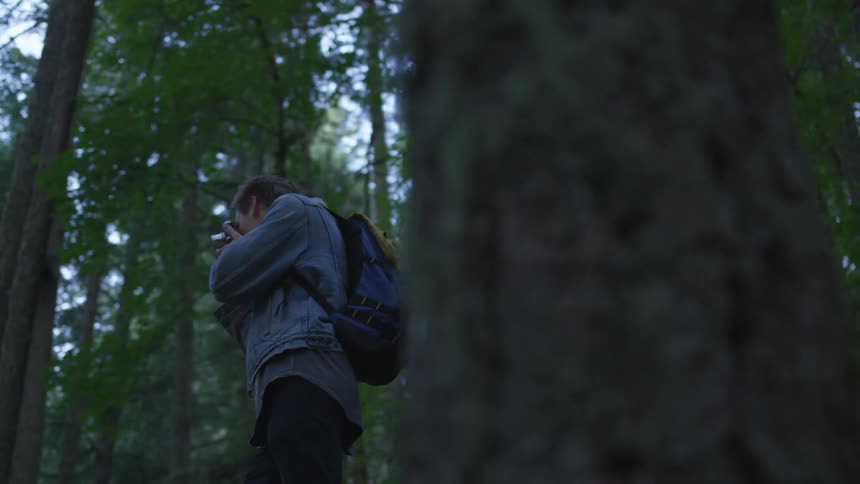 A man standing in a forest taking photos with a camera