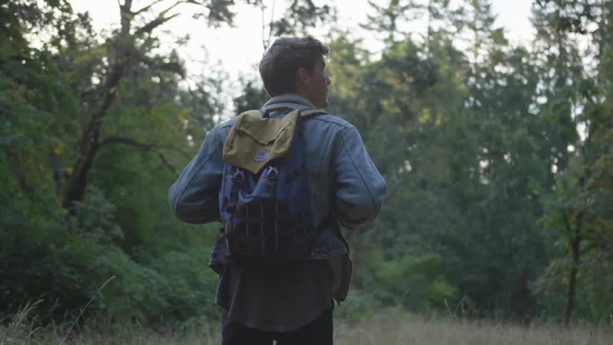 A man with a backpack on looking around in a forest on a trail