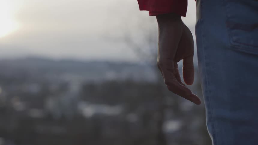 A person's hand and leg are seen as they stand still while overlooking a valley