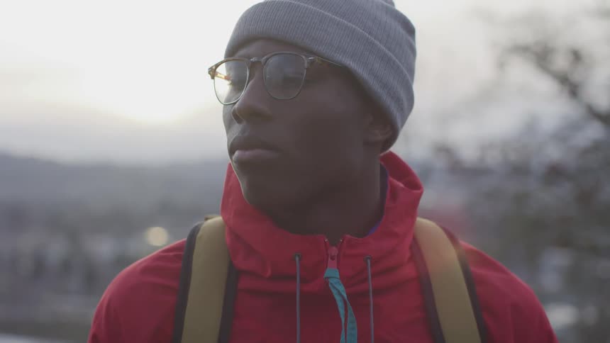 Man wearing beanie and glasses on hike looking side to side
