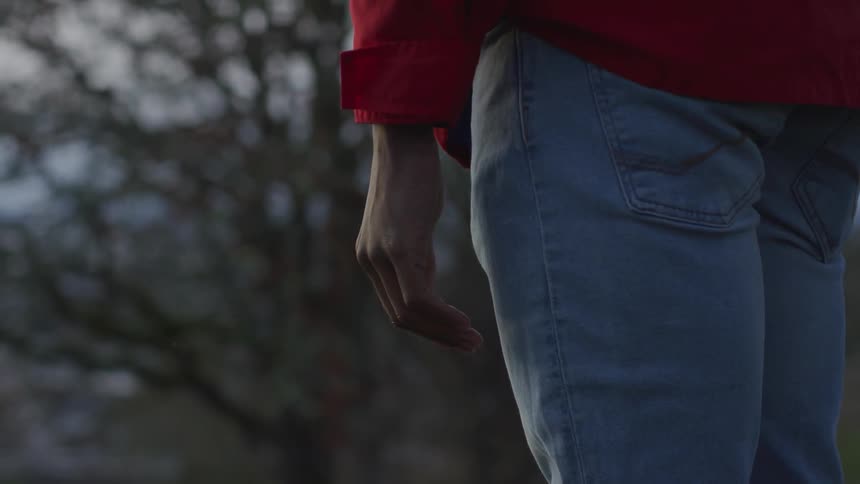 Person wearing blue jeans and red shirt stands with arms at their side